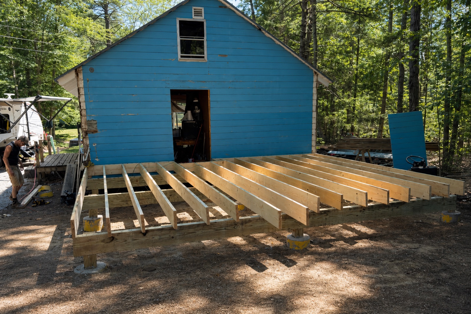 Jeff building the deck joist frame in front of the blue Canterbury cabin